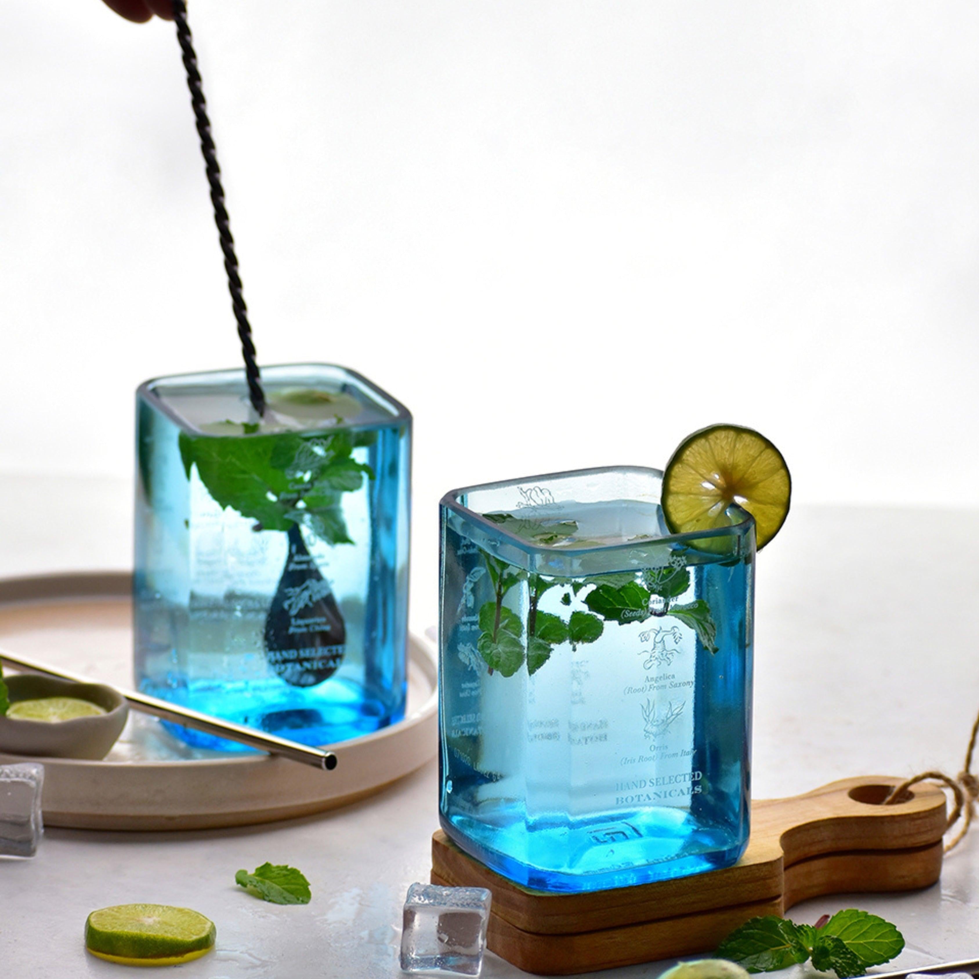 Two blue square glasses with a drink, lime slices, and mint leaves on a white background.